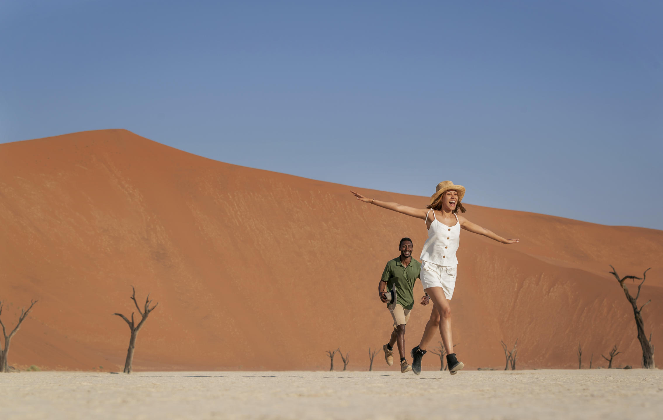 Guests exploring the striking white clay pan of Deadvlei, surrounded by towering red dunes in Sossusvlei, Namibia.